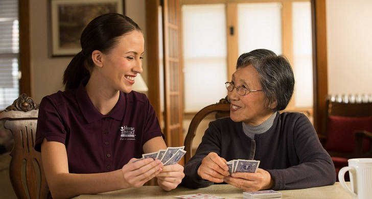 Caregiver and an elderly woman playing cards together.