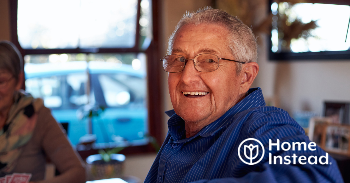 A smiling senior man is happy as a result of successful long-distance caregiving is sitting at a table and looking over his shoulder.