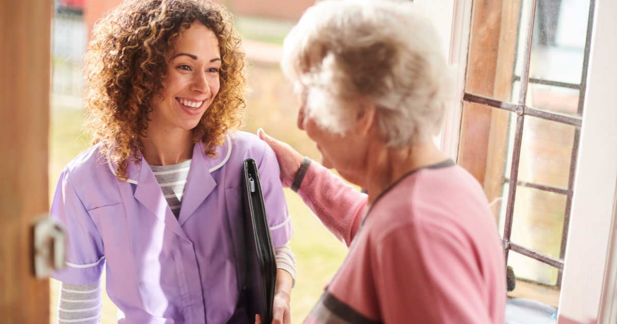 Smiling senior stands at the front door and welcomes a new caregiver into her home